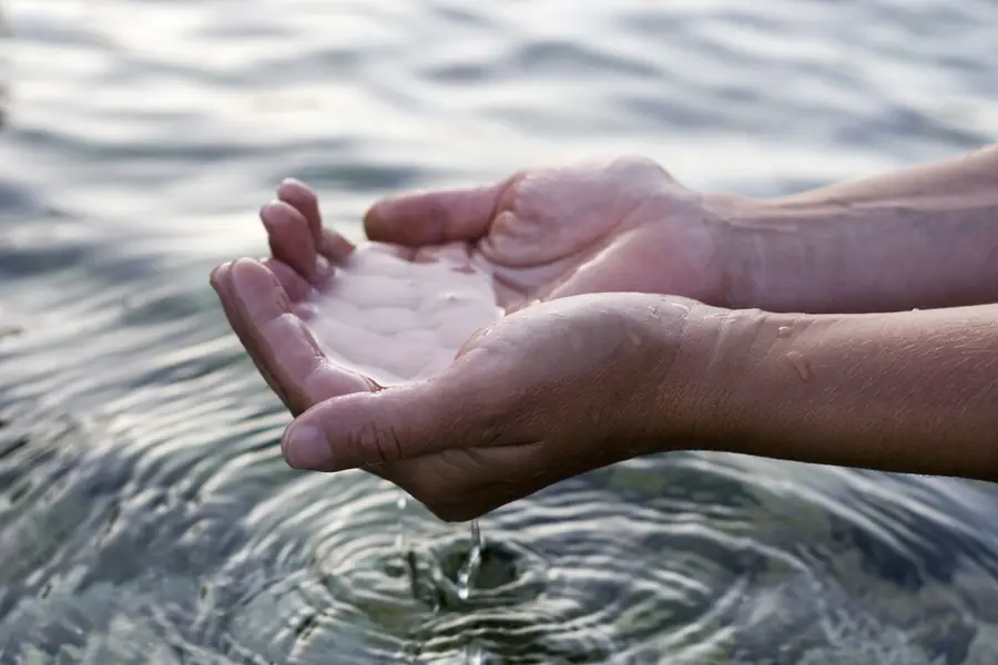 Hands cupping clear water above a rippling lake