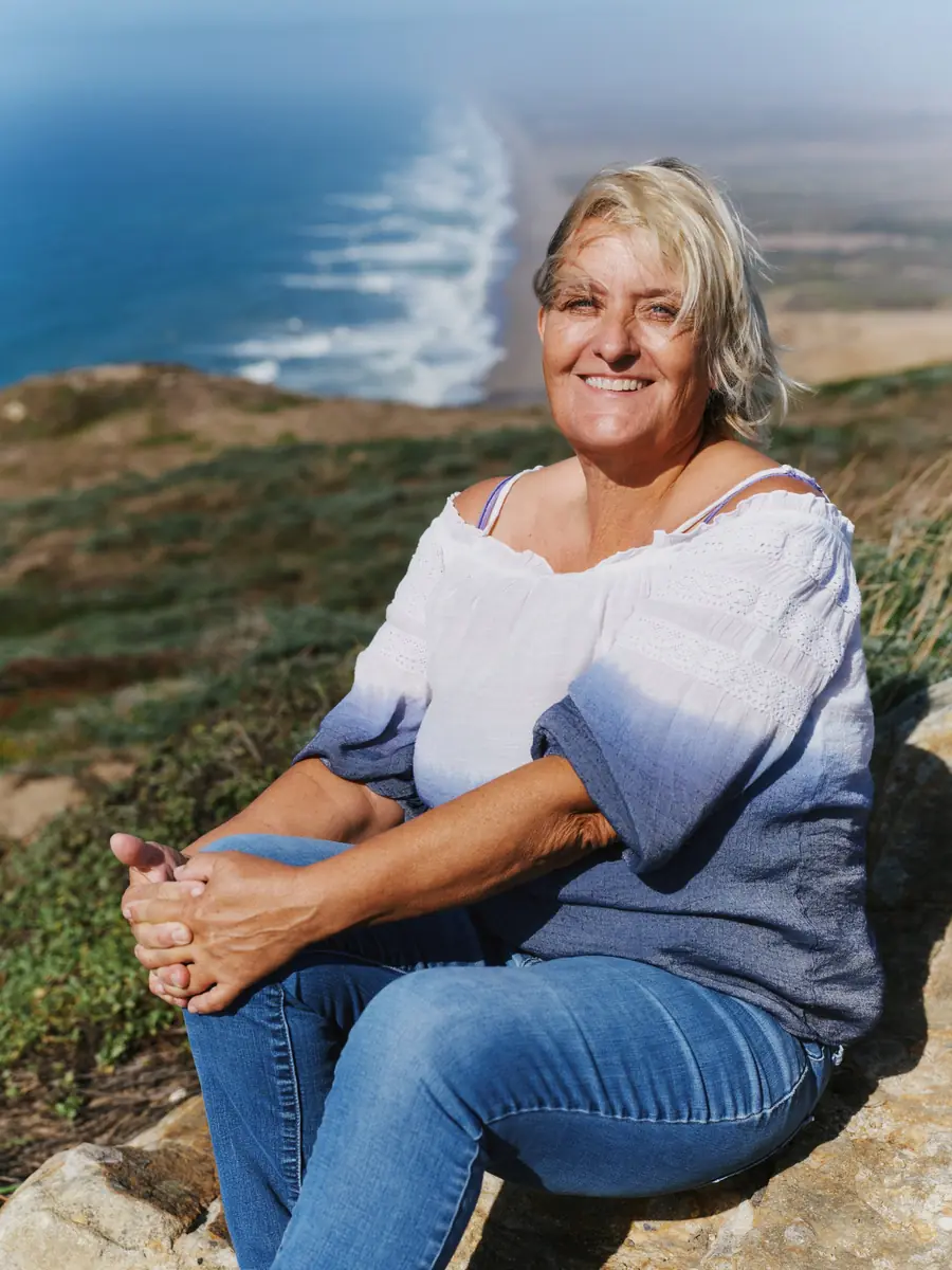 Heather Van Ness smiling, seated on a cliff above the Point Reyes coastline