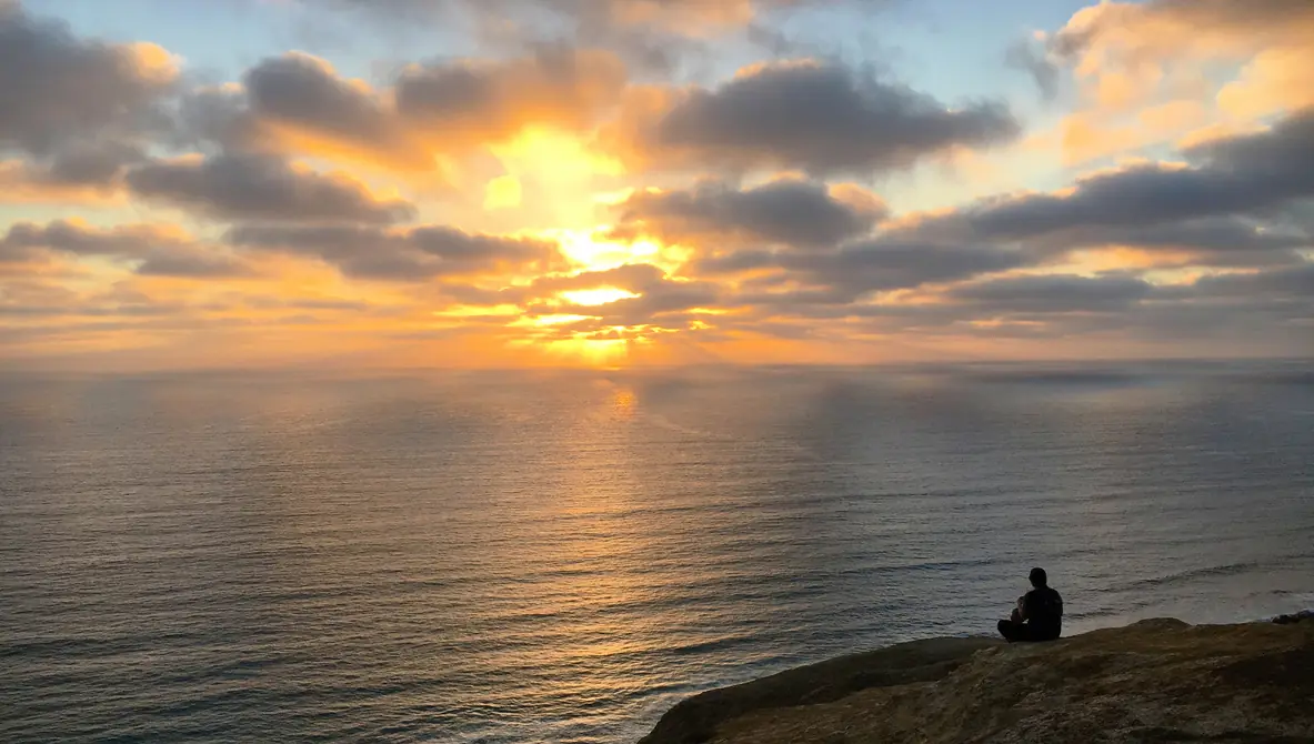 A person sitting on a cliff above the Pacific at sunset